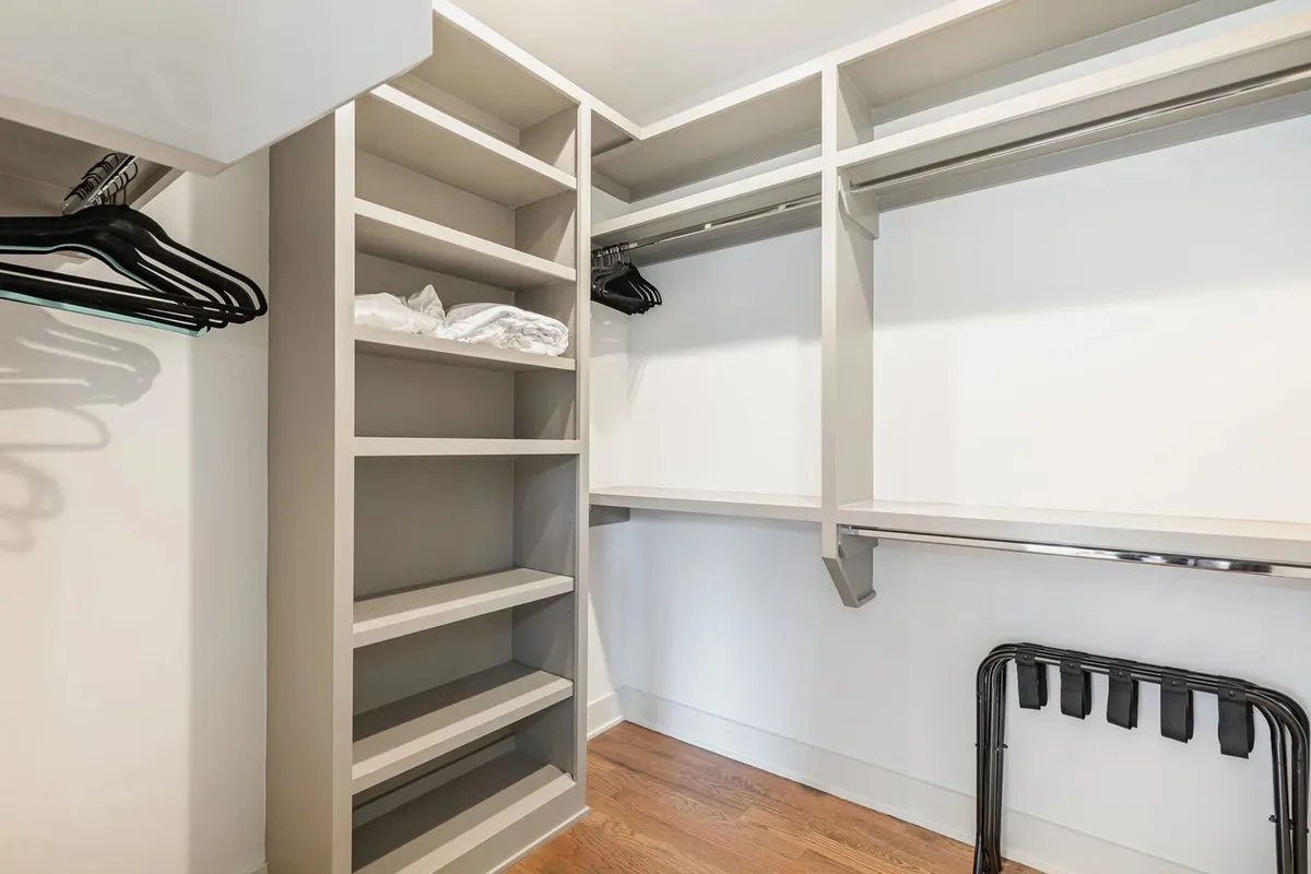 A minimalist, walk-in closet with open shelving, hanging rods, and a wooden floor, offering ample space for organizing clothes and accessories in a clutter-free environment.