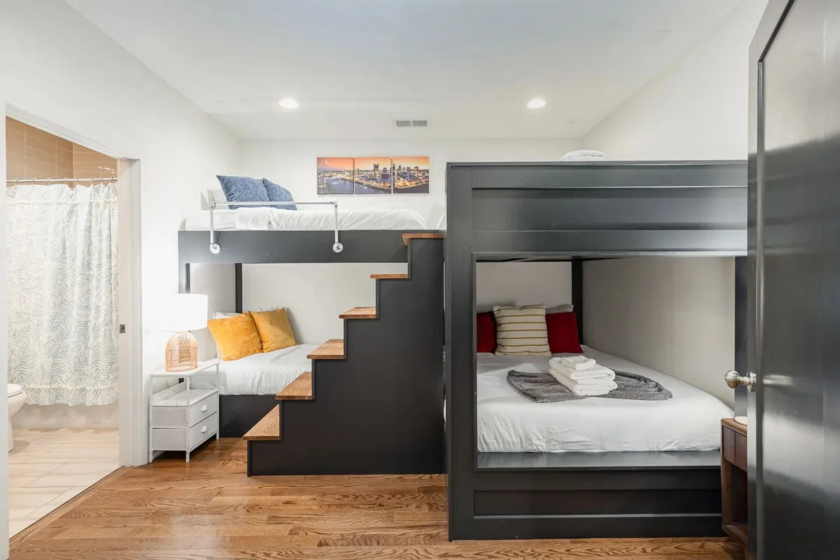 A playful bedroom with sturdy wooden bunk beds, a staircase for easy access, decorative wall art, and a cozy nightstand with a lamp, ideal for families or groups traveling with children.