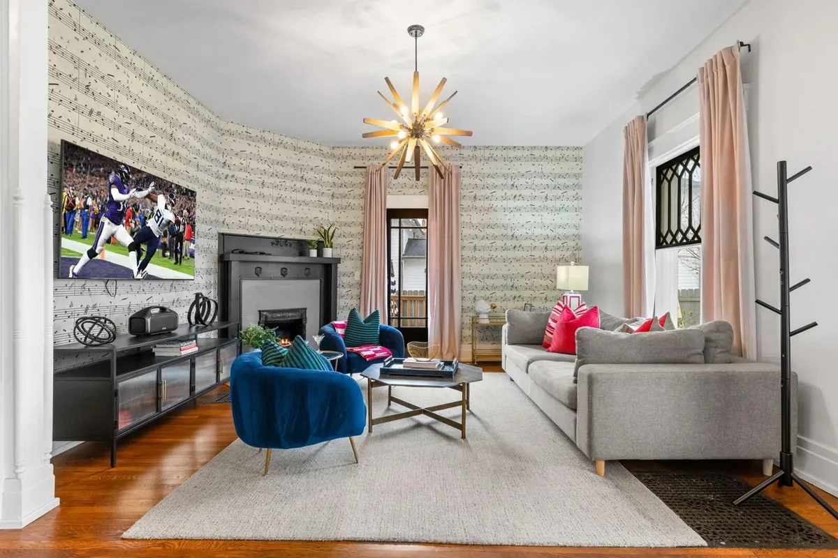 A lively living area equipped with musical note wallpaper, a modern chandelier, comfortable seating, and a large television. The layout is open, with multiple seating options for relaxation, socializing, or even casual work or play zones.