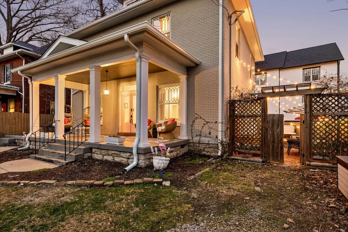 A front porch with decorative columns, a garden area, string lights, and a cozy outdoor seating arrangement. The atmosphere is welcoming and perfect for morning coffee or evening relaxation.