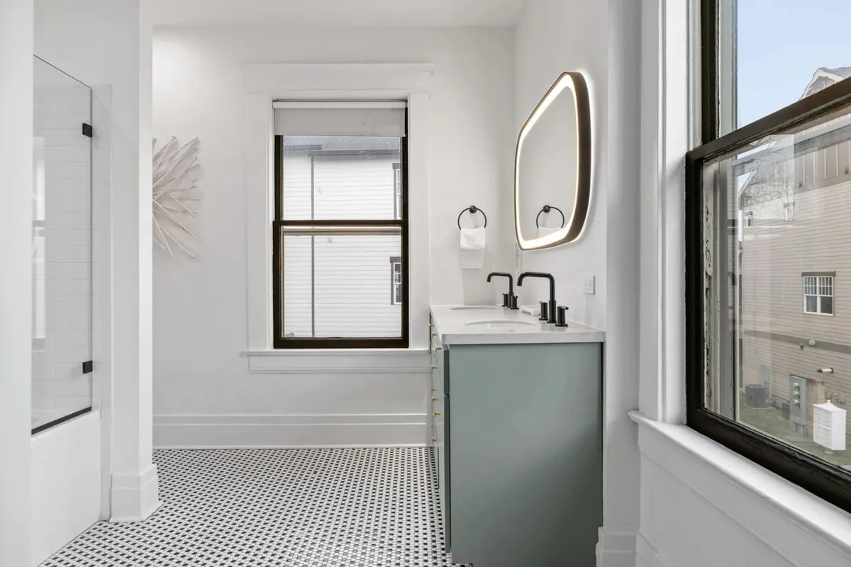 A spacious modern bathroom featuring a dual-sink vanity, large mirror with integrated lighting, contemporary fixtures, and decorative wall art, evoking a spa-like, tranquil atmosphere.