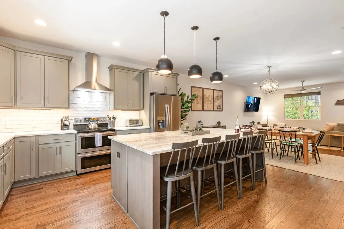 This image features a modern kitchen with a spacious island, pendant lighting, stainless steel appliances, and an adjacent dining area. The open design encourages both meal preparation and group interaction, making it ideal for gatherings.