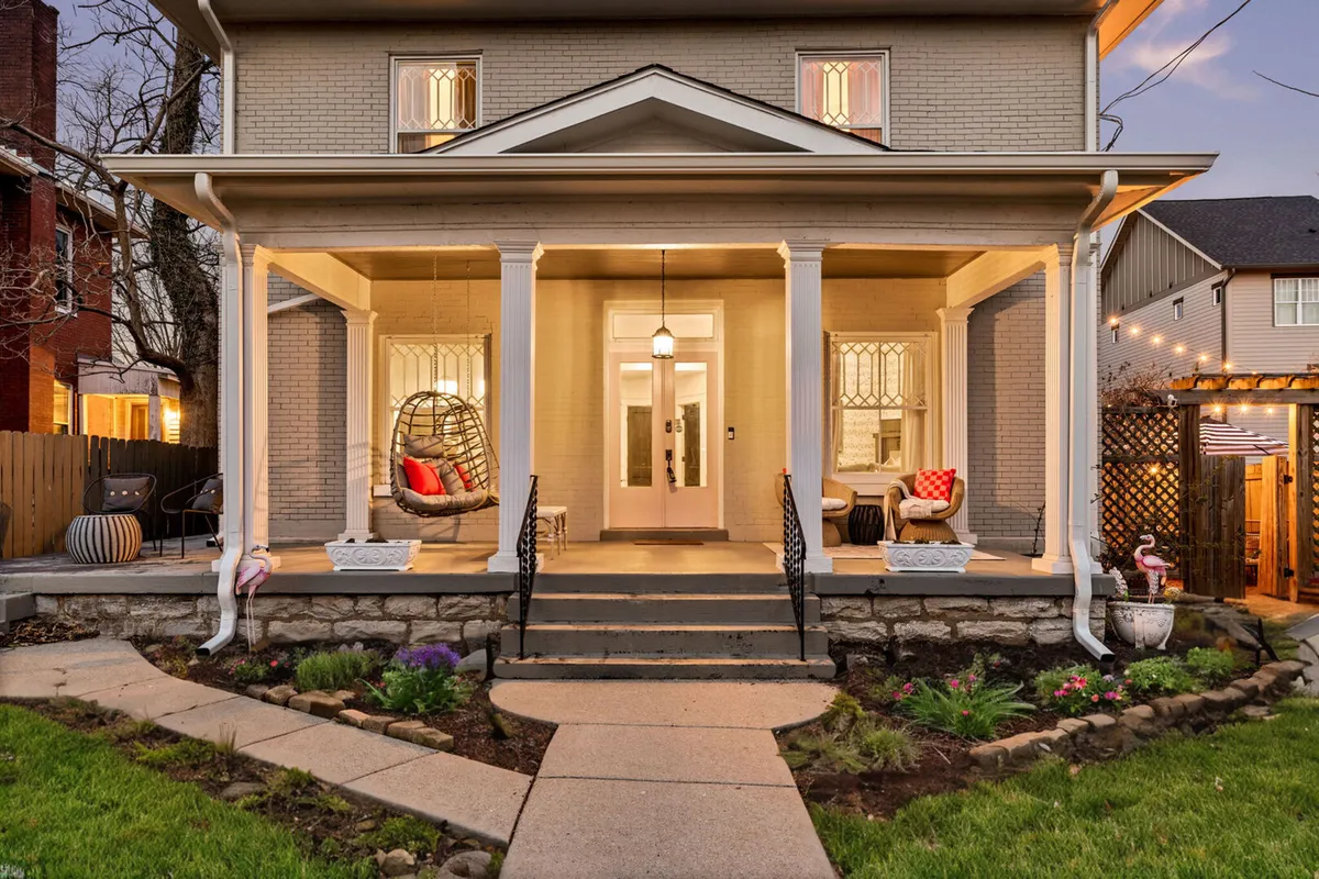 The image showcases the exterior of the Elegant Elliott, featuring a classic Southern-style front porch adorned with a cozy hanging chair, plush decorative pillows, and surrounded by a beautifully landscaped garden. The inviting setup hints at tranquil moments spent relaxing outdoors, socializing with friends, or enjoying a quiet evening sunset.